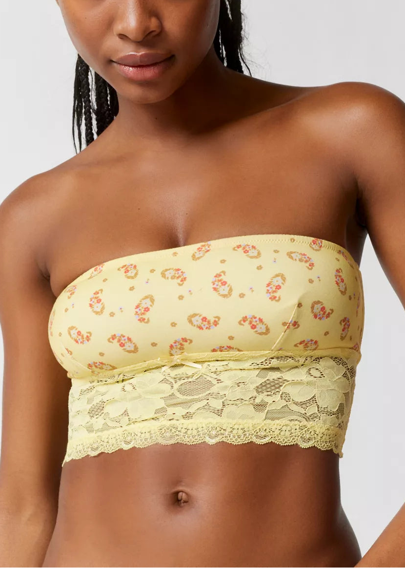 Woman wearing a yellow floral bandeau top with lace trim against a plain background