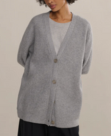 Person wearing a gray cardigan over a light gray shirt on a beige background
