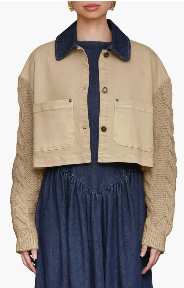 Person wearing a beige knitted jacket over a navy outfit on a white background