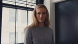 Woman in a gray sweater standing in a room with large windows