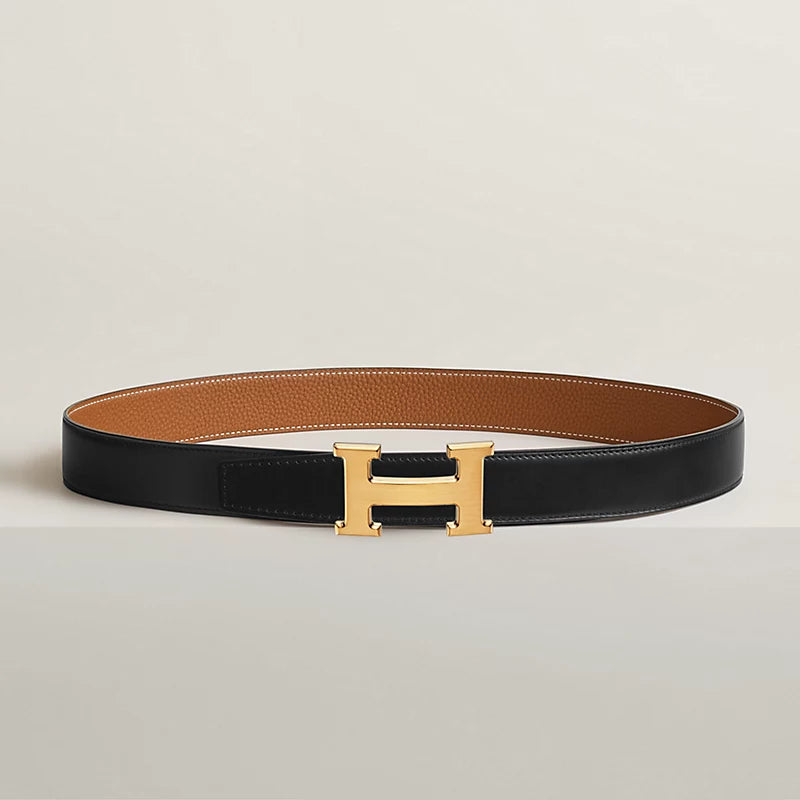 Black and brown leather belt with gold H-buckle on a light gray background