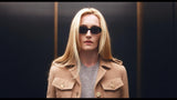 Person wearing sunglasses and a beige coat against a dark background