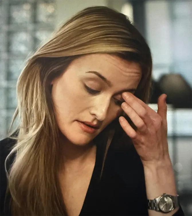 Woman with long blonde hair holding her face in a blurred indoor setting