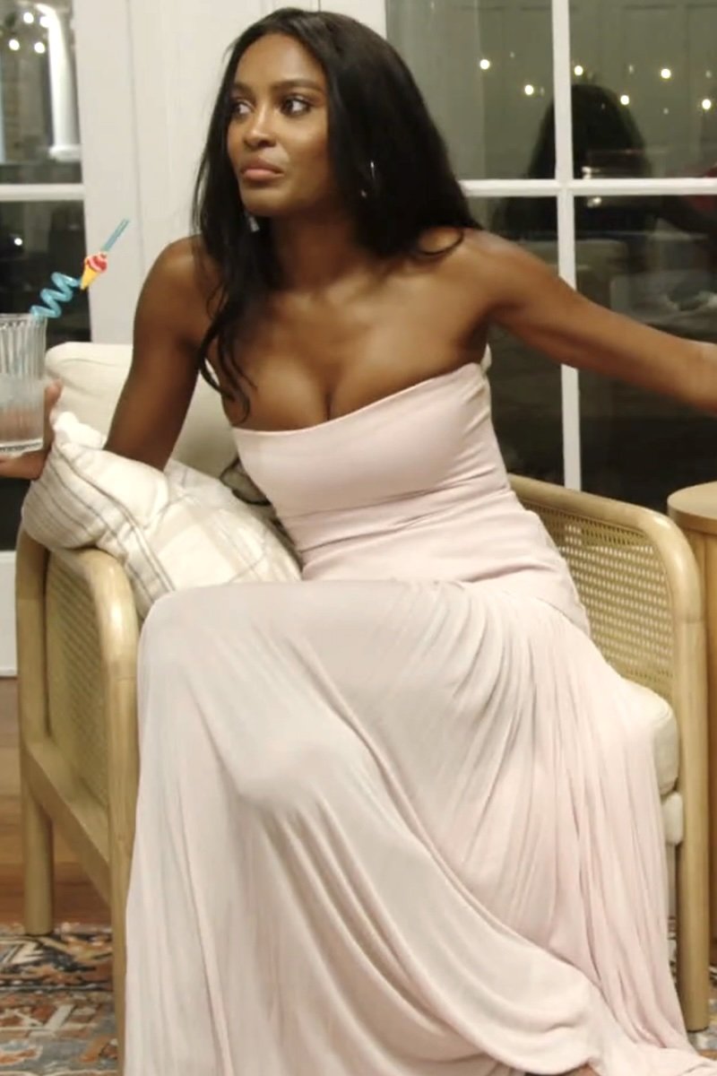 Woman in a light pink gown sitting on a chair indoors.