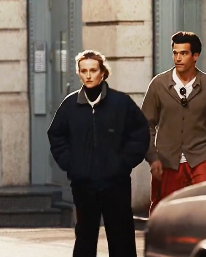 Two people standing on a street with cars and a building in the background