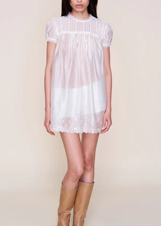 Woman wearing a white lace dress with brown boots on a plain background