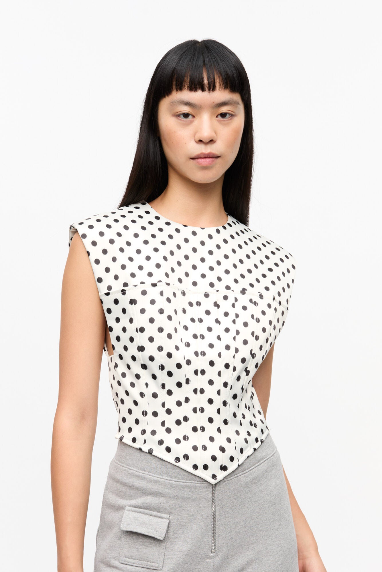 Woman wearing a sleeveless polka dot top and gray pants on a white background