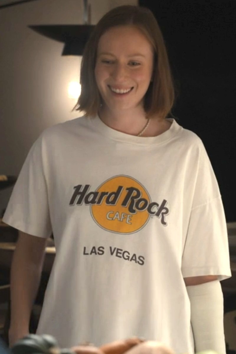 A woman wearing a white Hard Rock Cafe Las Vegas graphic t-shirt, smiling in a dimly lit indoor setting.
