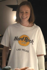 A woman wearing a white Hard Rock Cafe Las Vegas graphic t-shirt, smiling in a dimly lit indoor setting.