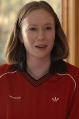 A woman with shoulder-length light brown hair wearing a red Adidas V-neck jersey with white piping, a black collar, and white embroidered text reading 'Mia Iron Banner' on the chest.