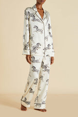 A model wearing a two-piece pajama set with a black and white zebra print on a cream background, standing against a solid beige backdrop.