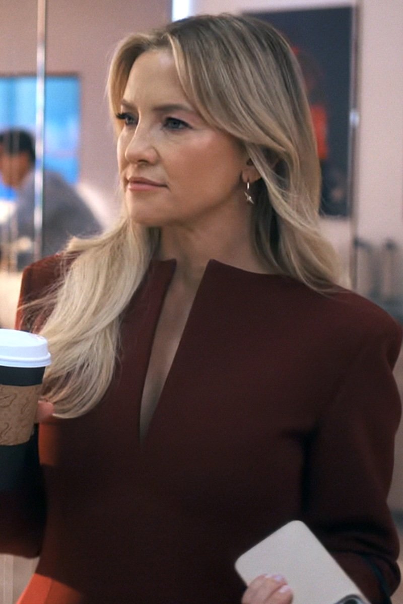 Woman in a maroon outfit holding a coffee cup and a white device, with a blurred background.