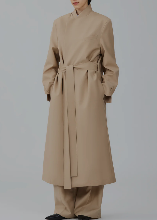 Person wearing a beige trench coat and pants on a plain background