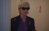 Person wearing sunglasses and a dark jacket with floral embellishments in an indoor setting.
