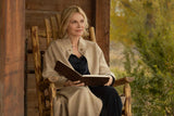 Woman sitting in a wooden chair reading a book outdoors.