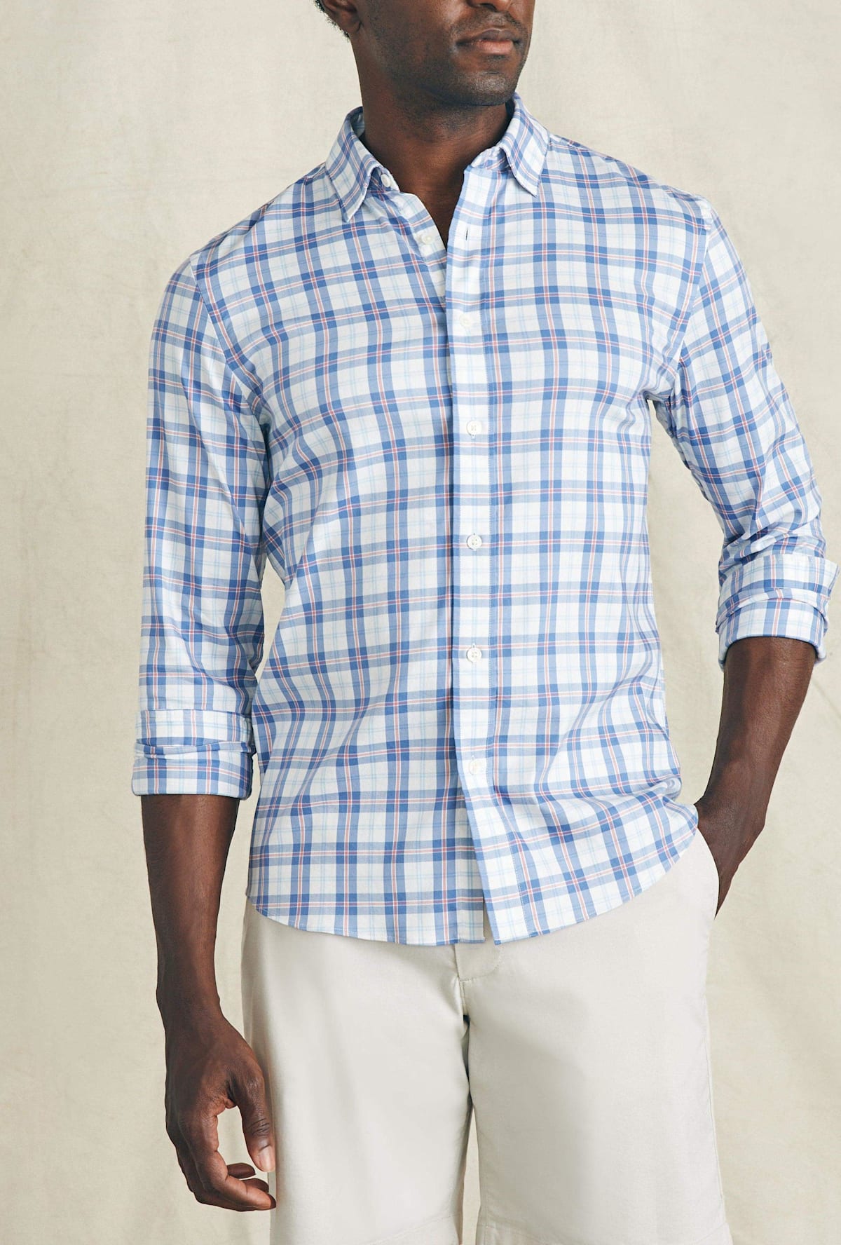 Man wearing a blue and white checkered shirt with rolled-up sleeves against a beige background