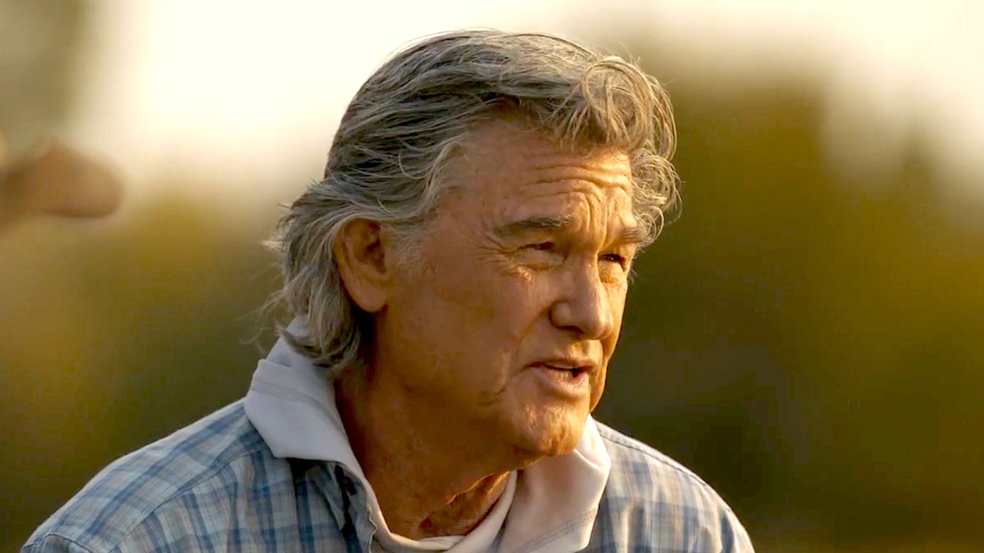 Man with gray hair wearing a plaid shirt against a blurred natural background