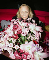 Person holding a large bouquet of pink flowers against a red background