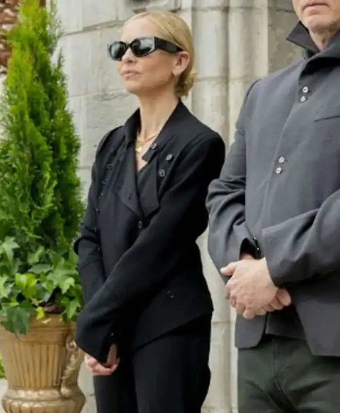 Two people in formal attire standing outdoors with a stone wall and greenery in the background.