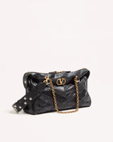 Black handbag with gold chain and logo on a light beige background