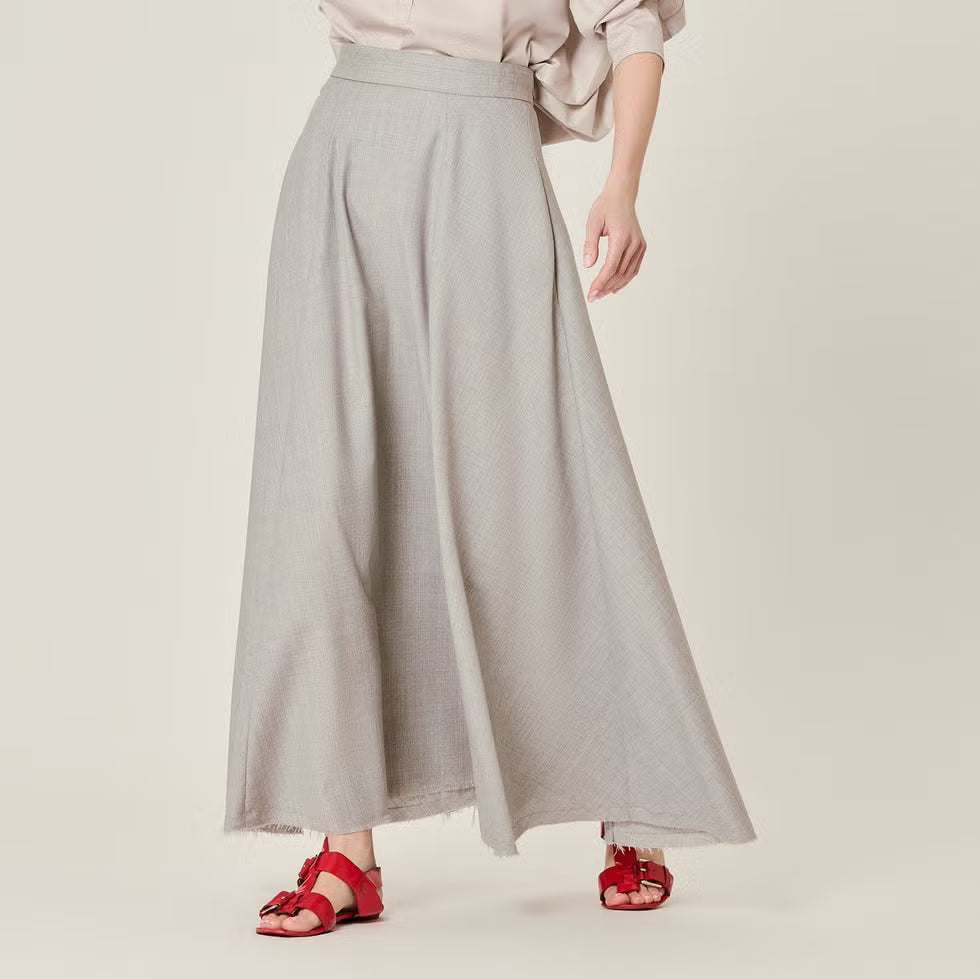 Person wearing a long gray skirt with red sandals on a plain background