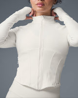 Woman wearing a white zip-up jacket against a gray background