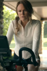 Woman in a white jacket standing on a porch with a camera setup in front of her.