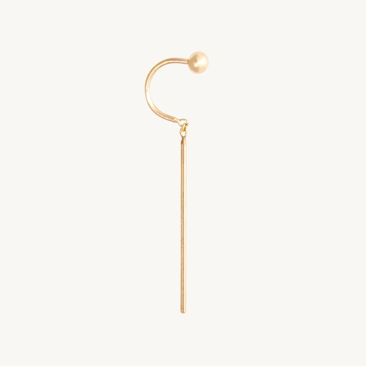 A gold-toned ear cuff earring featuring a curved hook with a small spherical bead at the top and a long straight drop, shown on a plain off-white background.