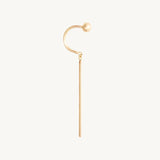 A gold-toned ear cuff earring featuring a curved hook with a small spherical bead at the top and a long straight drop, shown on a plain off-white background.