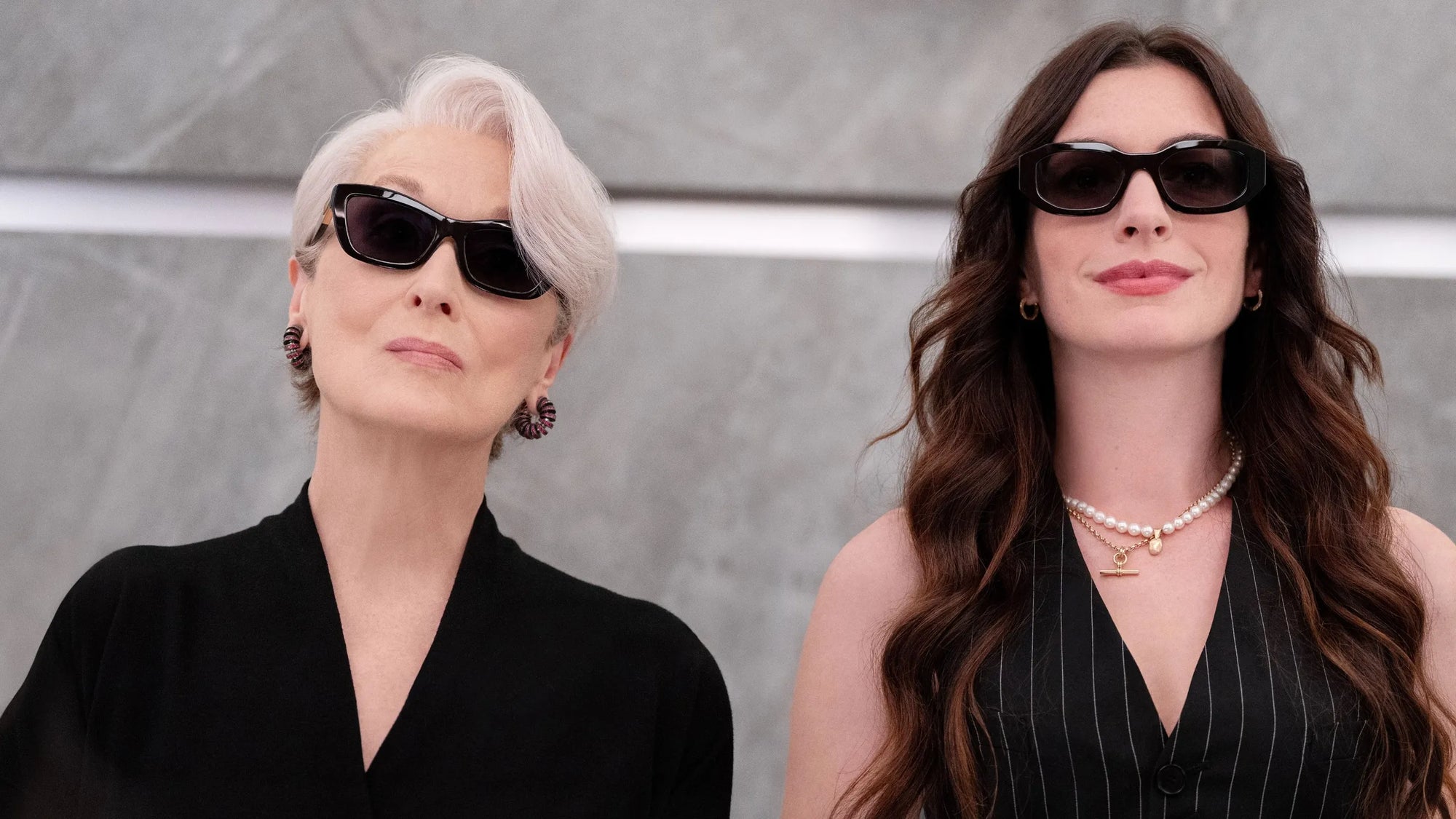 Two women wearing sunglasses against a gray background