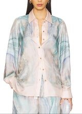 A model wearing a light pink button-up shirt with a blue and green marble print, paired with matching printed pants, against a plain white background.