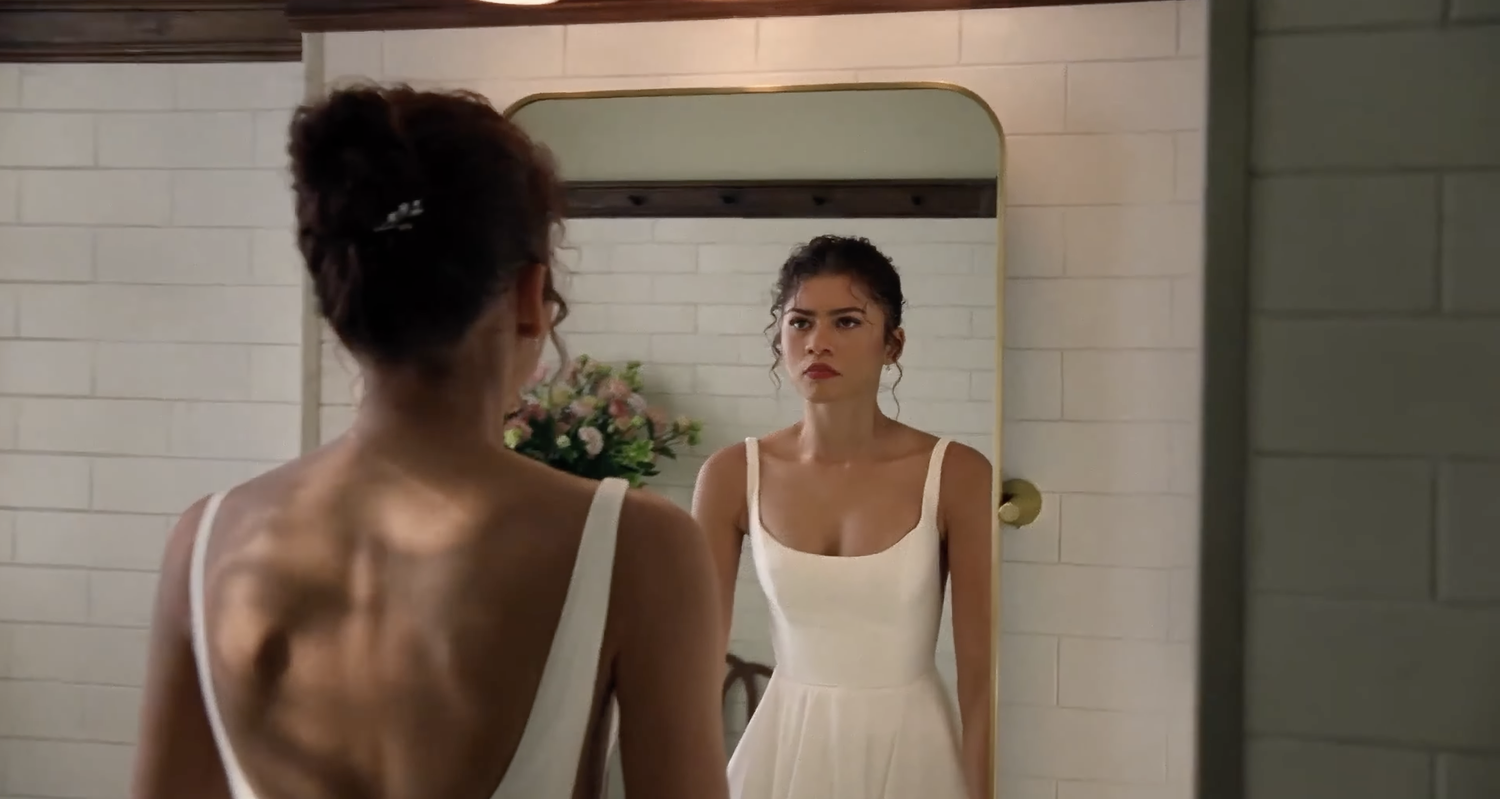 Woman in a white dress standing in front of a mirror in a bathroom.